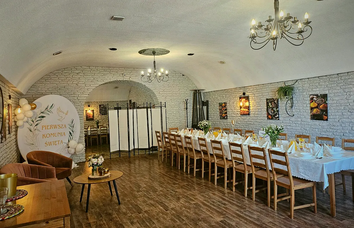 Sala Pizzerii Verona w Redzie przygotowana na komunię: długi stół z białymi obrusami i kwiatami, żyrandole i ścianka z napisem Pierwsza Komunia Święta